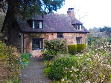 A stone cottage with a tiled roof surrounded by plants and bushes at Saint Pancras Chapel in Washford near Williton