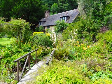 A garden with a wooden bridge and flowers in front of a cottage in Saint Pancras Chapel Washford near Williton