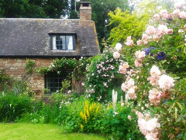 A stone cottage with flowering plants and green lawn in a garden at Saint Pancras Chapel in Washford near Williton