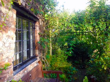 A garden with a wooden bench next to a stone building and a trellis covered with green plants at Saint Pancras Chapel in Washford near Williton