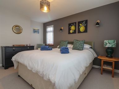 A bedroom with a large bed with white bedding and blue towels on it two green pillows two paintings above the bed and bedside table with a lamp