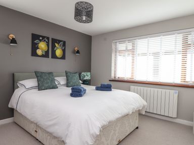 A bedroom with a bed with white bedding green pillows and blue towels near a window with white blinds at Stonecroft in Praa Sands