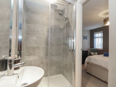 A bathroom with a shower area and a sink next to a bedroom with a bed and a nightstand at Stonecroft in Praa Sands