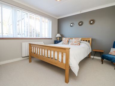 A bedroom with a wooden bed frame white bedding pillows a side table with a lamp blue chair and three round mirrors on a gray wall at Stonecroft Praa Sands