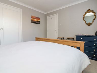 A bedroom with a wooden bed frame white bedding a blue dresser with stools and a decorative mirror at Stonecroft in Praa Sands