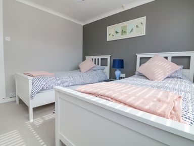 A bedroom with two single beds side by side with white frames and blue and white bedding with pink blankets and pillows at Stonecroft in Praa Sands