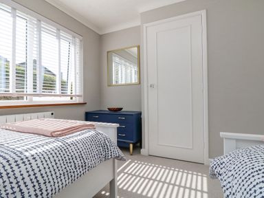 A bedroom with two beds a blue chest of drawers a mirror and a window with blinds at Stonecroft Praa Sands