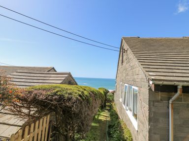 A side view of a stone house with a hedge and a gate overlooking the sea at Stonecroft in Praa Sands