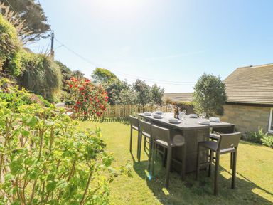An outdoor dining table with chairs set with plates and glasses in a garden near a house at Stonecroft in Praa Sands