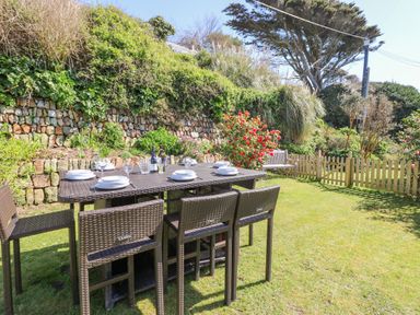 An outdoor dining area with a table set with plates and glasses on a lawn with plants and a stone wall in the background at Stonecroft in Praa Sands