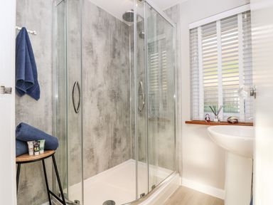 A bathroom with a glass shower enclosure towels on a stool and a sink by a window at Stonecroft in Praa Sands