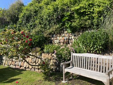 A garden with a stone wall and a wooden bench at Stonecroft in Praa Sands