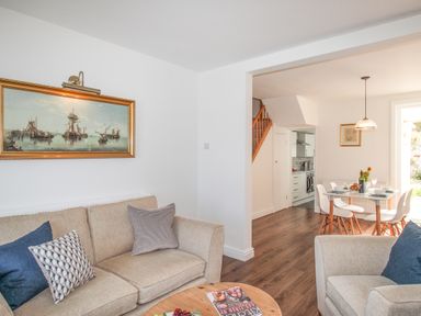 A living room with beige sofas and pillows and a painting on the wall next to a dining area with a table and chairs at The Shambles in Fortuneswell
