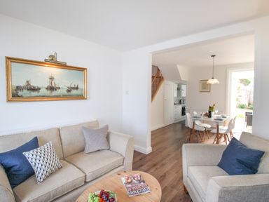 A living room with sofas and cushions a round wooden coffee table and painting looking into a dining area with a table and chairs at The Shambles in Fortuneswell