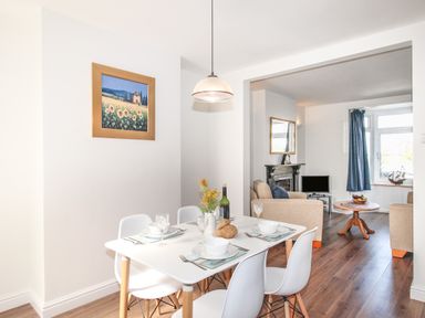 A dining area with a white table set for four next to a living room with beige sofas and a round wooden coffee table at The Shambles in Fortuneswell