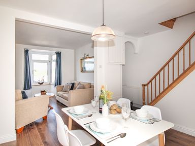 A dining table set with bowls and plates next to a staircase and a living room with sofas and a window with curtains at The Shambles in Fortuneswell