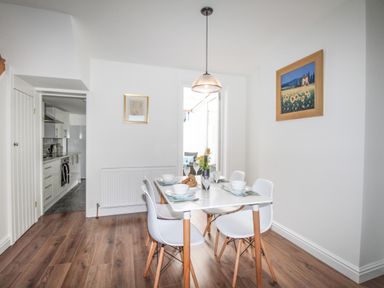 A dining area with a table set for four and white chairs next to a kitchen at The Shambles in Fortuneswell