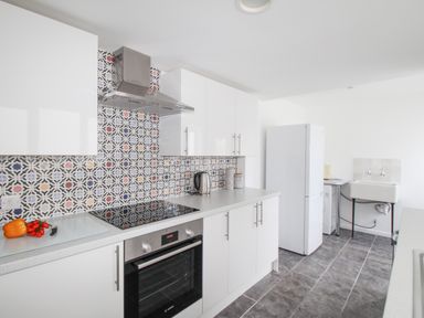 A kitchen with white cabinets a black oven a patterned tile backsplash a white refrigerator and a utility sink at The Shambles in Fortuneswell