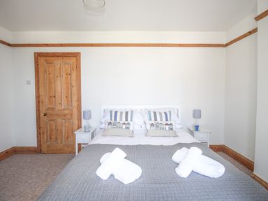 A bedroom with a bed with pillows and folded towels two bedside tables with lamps and a wooden door at The Shambles in Fortuneswell