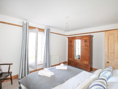 A bedroom with a bed, wooden wardrobe, chair, window with curtains, and a wooden door at The Shambles in Fortuneswell
