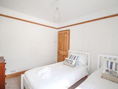 A bedroom with two single beds with white frames and bedding a wooden door and a wooden dresser at The Shambles in Fortuneswell