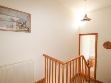 A staircase with wooden handrails leading to a hallway with a basket and framed picture on the wall at The Shambles in Fortuneswell
