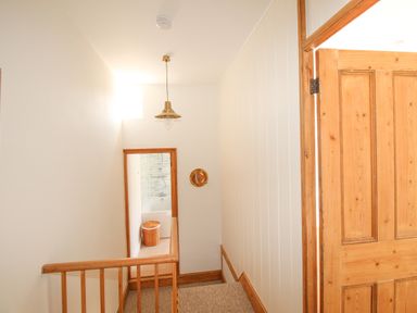 A staircase leading down to a bathroom visible through a wooden door frame with a wicker basket and bathtub at The Shambles in Fortuneswell