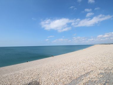A pebble beach with a few people near the water and a blue sea under a sky with clouds at The Shambles in Fortuneswell