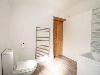 A bathroom with a toilet a heated towel rail a wooden door and a bathtub with tiled wall at The Shambles in Fortuneswell