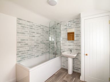 A bathroom with a bathtub shower combination sink mirror and a door at The Shambles in Fortuneswell