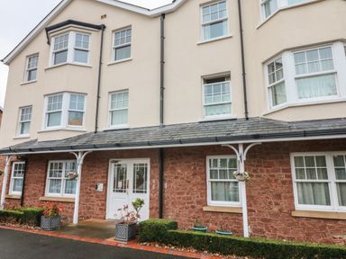 The exterior of a residential building with multiple windows a double door entrance flower pots and hanging baskets at 1 Tregonwell Court in Minehead