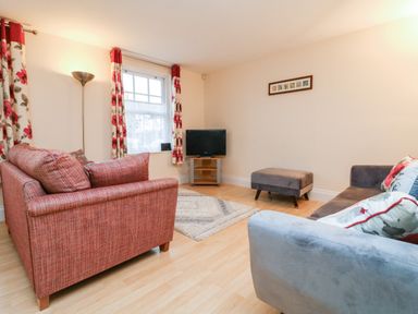 A living room with red and gray sofas a television on a stand a floor lamp and floral curtains at 1 Tregonwell Court in Minehead