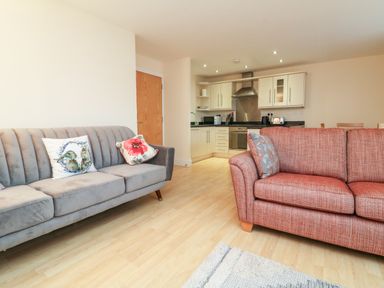 A living area with two sofas and an open kitchen with appliances and cabinets at 1 Tregonwell Court in Minehead