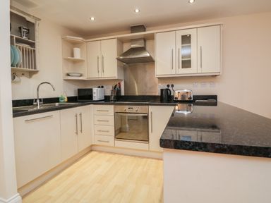 A kitchen with white cabinets black countertops a stainless steel oven and extractor fan at 1 Tregonwell Court Minehead