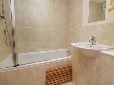 A bathroom with a bathtub a shower head a sink and a mirror at 1 Tregonwell Court in Minehead