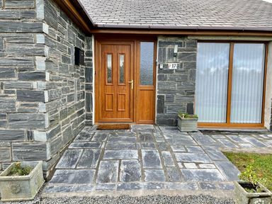 A stone front entrance with a wooden door two planters and a large window at Yr Encil in Llanddaniel near Gaerwen