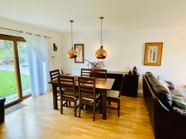 A dining area with a wooden table six chairs copper pendant lights and a sliding glass door at Yr Encil in Llanddaniel near Gaerwen