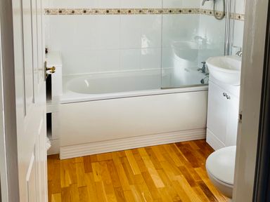 A bathroom with a bathtub shower combination a white sink with cabinet and a toilet at Yr Encil in Llanddaniel near Gaerwen