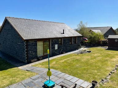 A backyard with a stone house patio lawn a table with chairs and a portable game at Yr Encil in Llanddaniel near Gaerwen