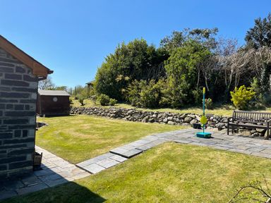 A garden with a stone path a bench a dartboard on a shed and a grassy area at Yr Encil in Llanddaniel near Gaerwen