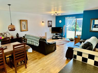 A living room with leather sofas wooden dining table and chairs a corner TV and sliding glass doors at Yr Encil in Llanddaniel near Gaerwen