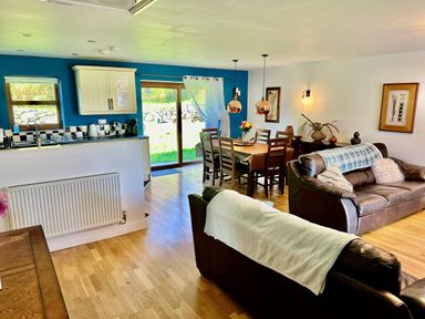 An open plan living room and kitchen with leather sofas a dining table and glass sliding doors at Yr Encil in Llanddaniel near Gaerwen