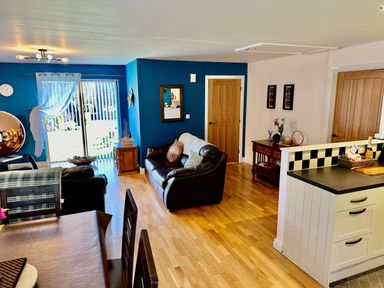 A dining table with chairs next to a living room with sofas and a wooden door at Yr Encil in Llanddaniel near Gaerwen