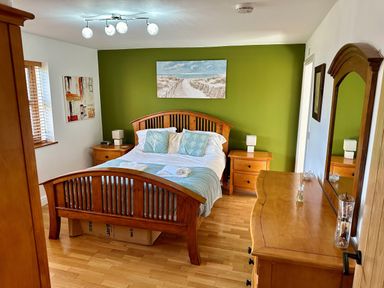 A bedroom with a wooden bed flanked by two wooden nightstands and a wooden dresser with a mirror at Yr Encil in Llanddaniel near Gaerwen