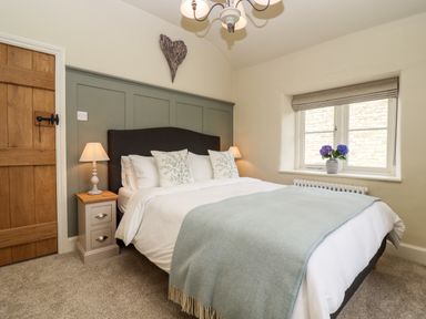 A bedroom with a bed bedside tables lamps and a window with flowers on the sill at 4 Lower Folley in Chipping Campden