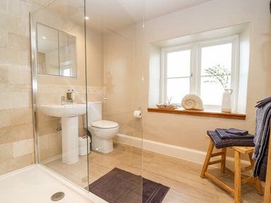 A bathroom with a shower area sink and toilet next to a window with towels on a stool at 4 Lower Folley in Chipping Campden