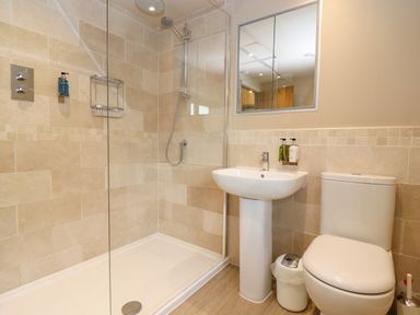 A bathroom with a shower area sink toilet mirror and small trash bin at 4 Lower Folley in Chipping Campden