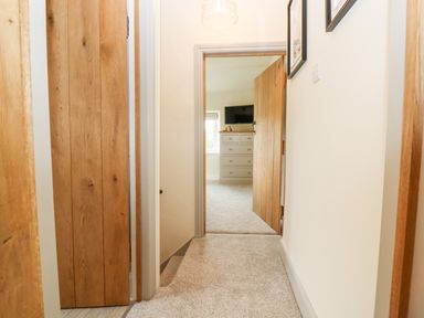 A carpeted hallway with wooden doors leading to a room with a chest of drawers and a wall-mounted television at 4 Lower Folley in Chipping Campden