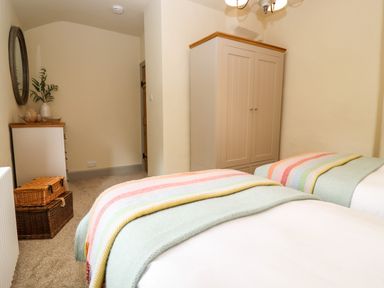 A bedroom with two beds covered with blankets a wardrobe a chest of drawers with decorations and a large round mirror on the wall at 4 Lower Folley in Chipping Campden