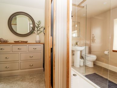 A dresser with a round mirror above it next to a bathroom with a toilet sink and glass shower screen at 4 Lower Folley in Chipping Campden